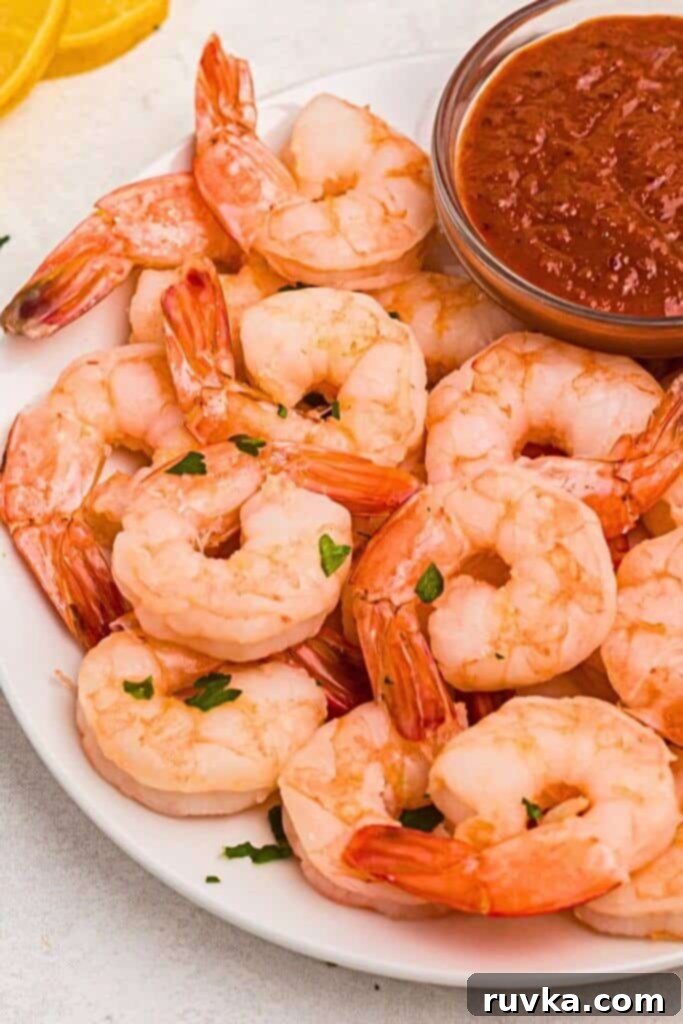 Easy Air Fryer Frozen Shrimp 6 Orange juicy shrimp on a white plate with cocktail sauce and lemon wedges for garnish.