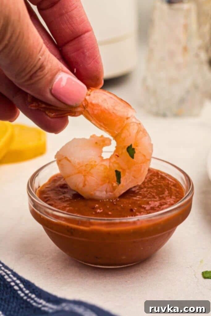 Easy Air Fryer Frozen Shrimp 7 Juicy orange shrimp being dipped into cocktail sauce, highlighting its readiness for enjoyment.
