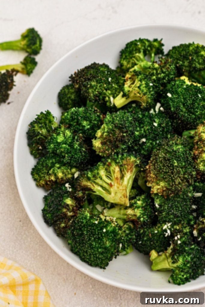 Crispy Air Fryer Broccoli 2 Green seasoned broccoli in a white bowl on a marble table.