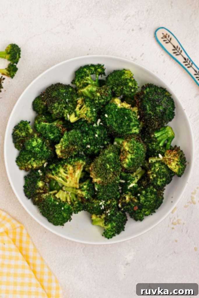 Crispy Air Fryer Broccoli 6 Bright green cooked broccoli in a white bowl sprinkled with seasonings and cheee.