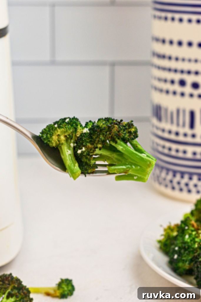 Crispy Air Fryer Broccoli 7 Green seasoned broccoli florets on a fork in front of an air fryer.