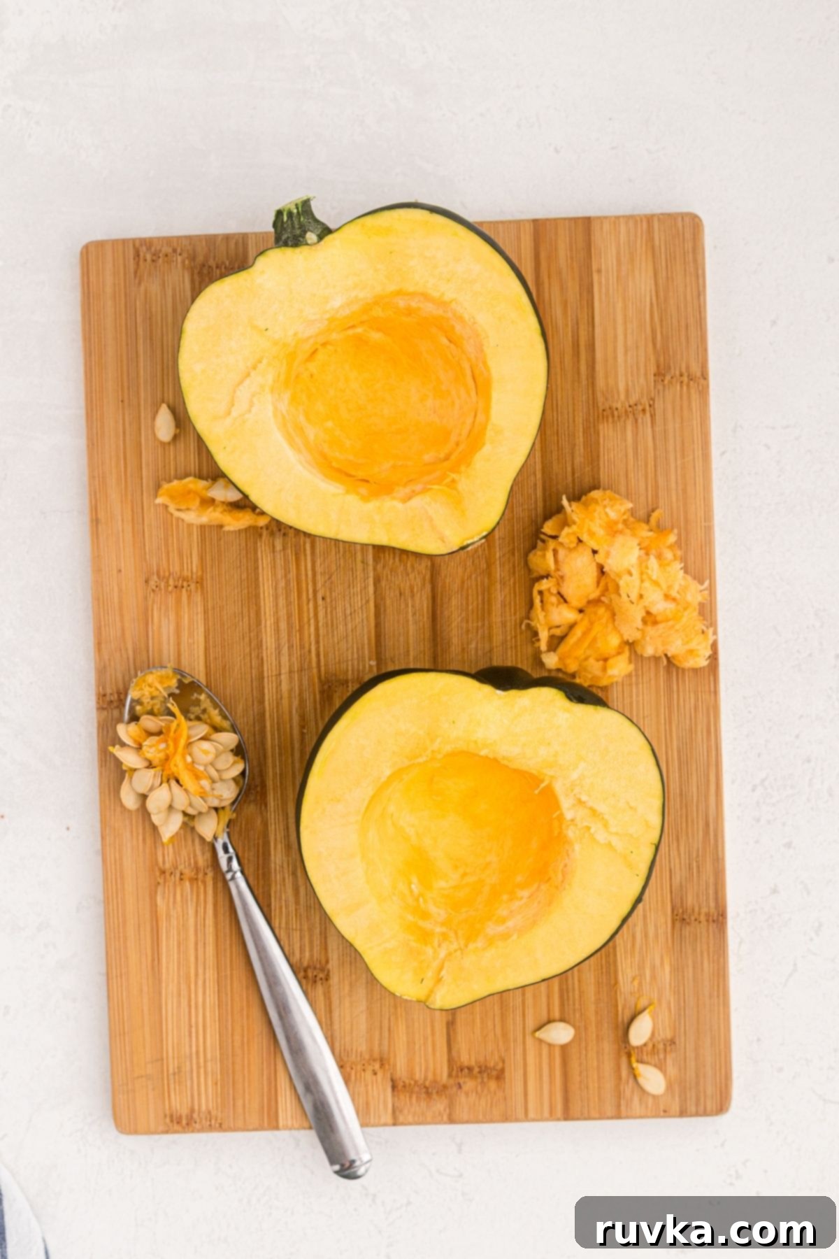 Crispy Air Fried Acorn Squash 4 Acorn squash cut in half with a spoon scooping out seeds on a wooden cutting board
