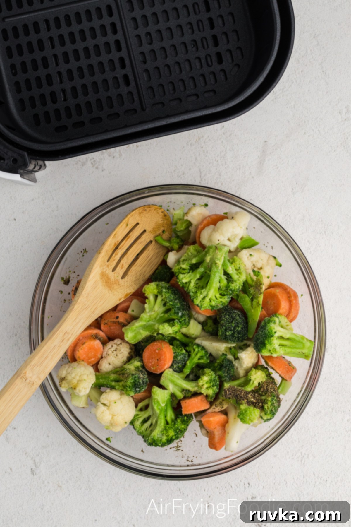 Crispy Air Fried Frozen Vegetables 4 A bowl of frozen mixed vegetables being tossed with avocado oil and seasonings (garlic powder, onion powder, salt, pepper) before air frying.