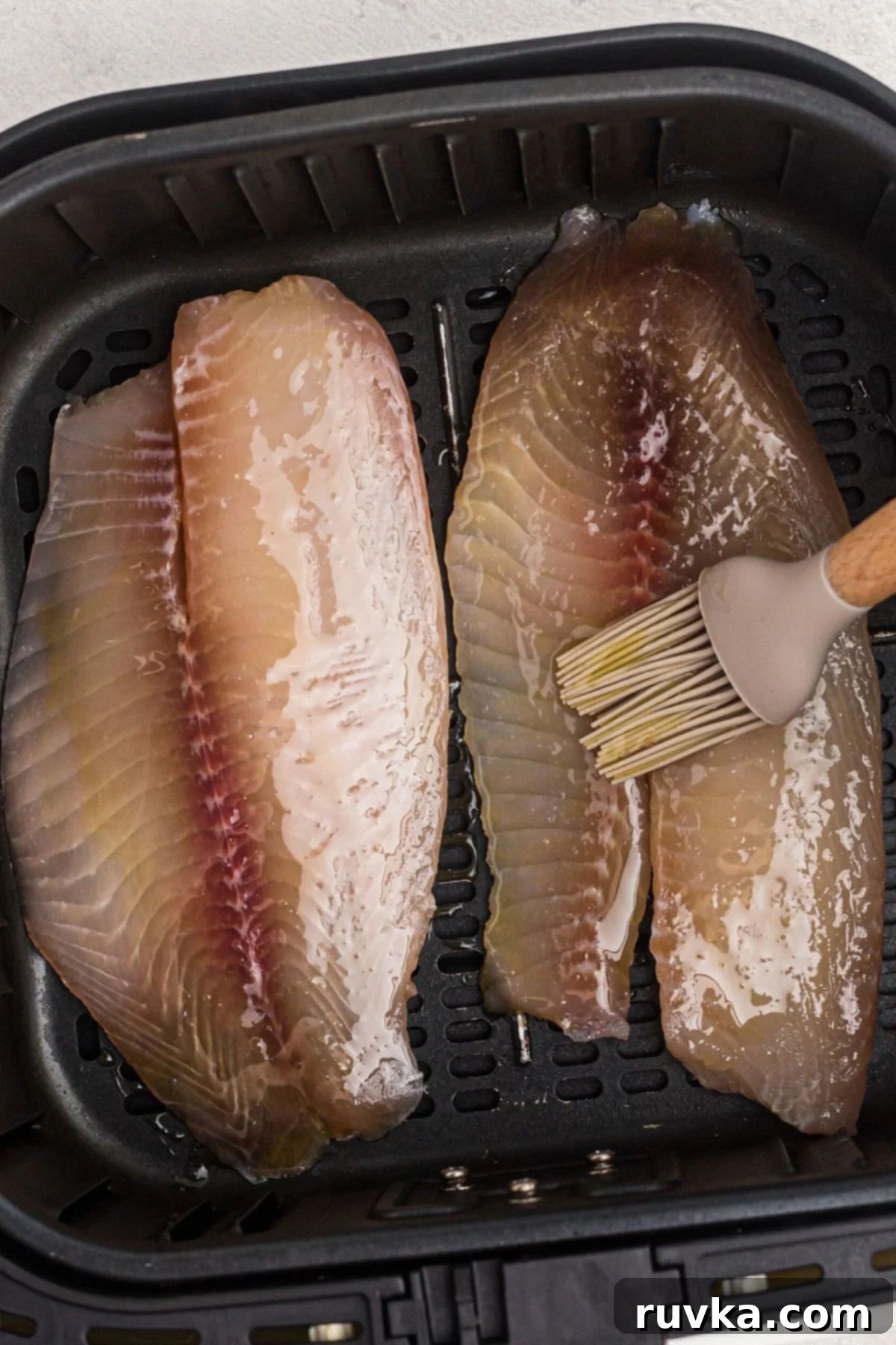 Crispy Air Fryer Tilapia 4 brushing oil onto fish filets before seasoning and cooking