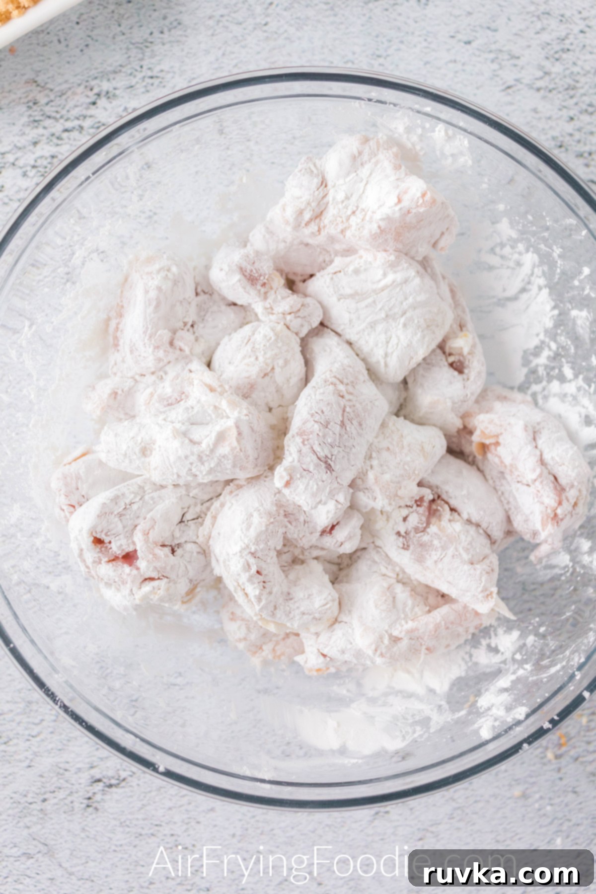 Crispy Golden Air Fryer Sesame Chicken 4 chicken tossed in cornstarch and flour in a glass bowl.