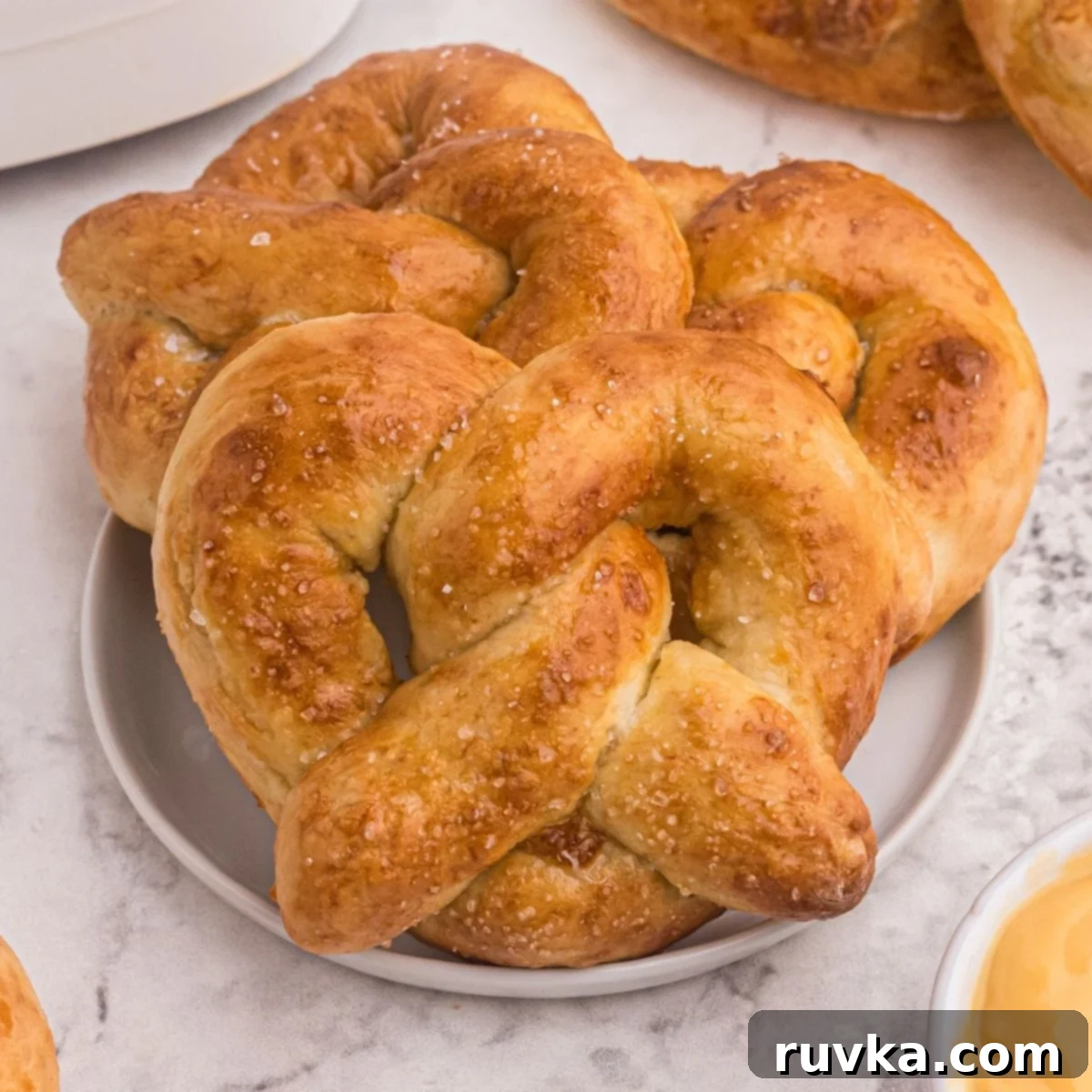 Super Bowl Air Fryer Snacks 16 Golden, fluffy soft pretzels, generously sprinkled with sea salt and served with melted cheese for dipping, on a white plate.