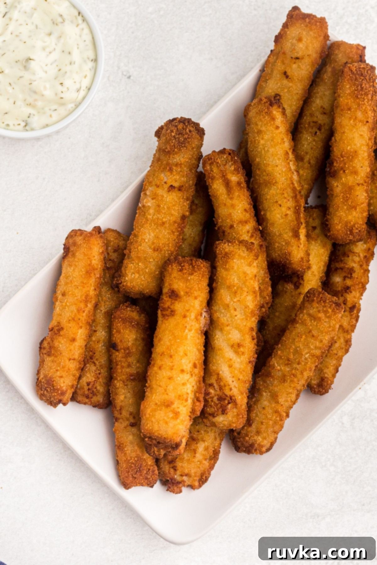 Super Bowl Air Fryer Snacks 21 Golden, crispy air fryer fish sticks neatly arranged on a white plate, ready to be served with dipping sauce.