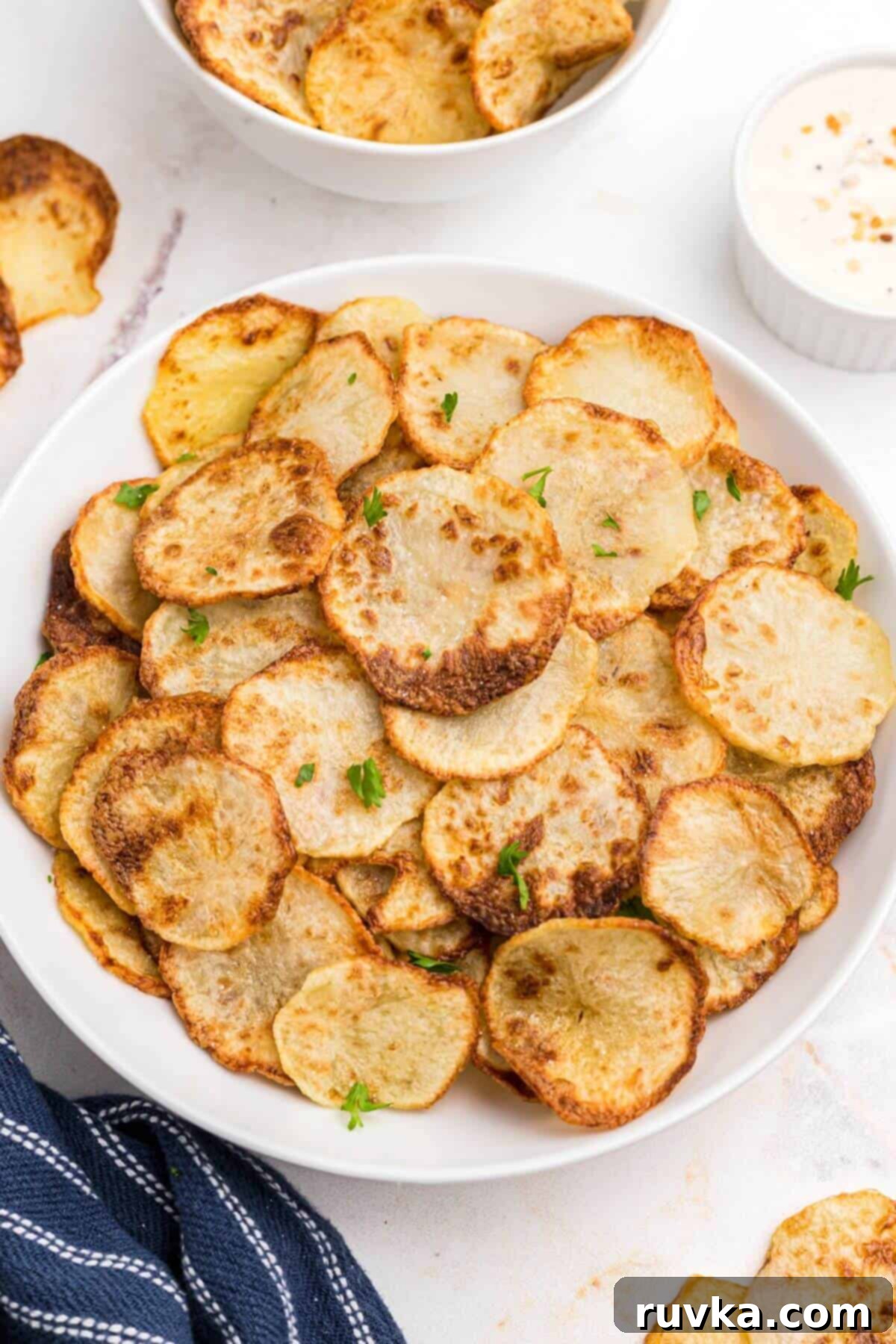 Super Bowl Air Fryer Snacks 24 Golden yellow crispy potato chips, freshly made in the air fryer, stacked invitingly in a white bowl.