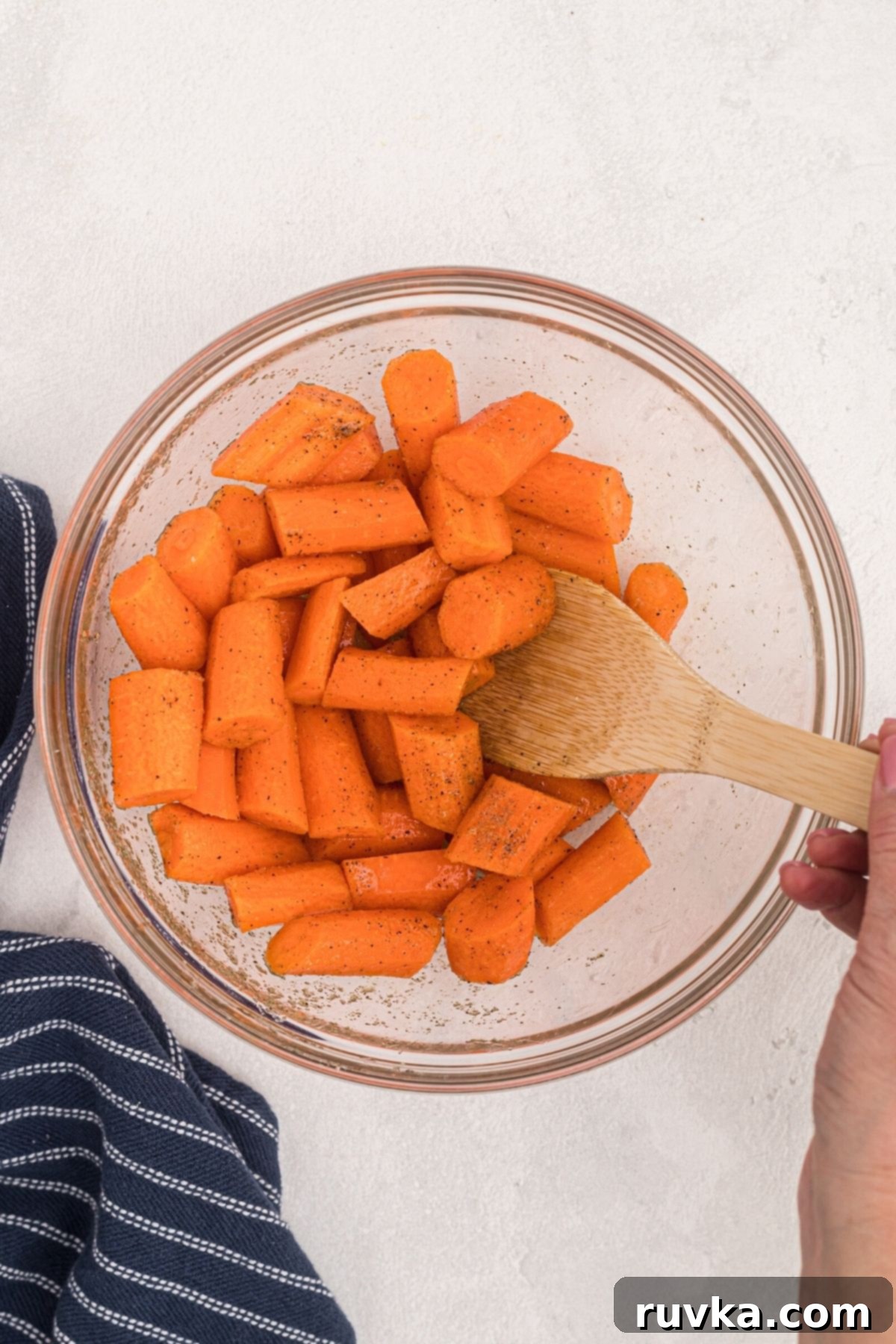 Golden Air Fryer Carrots 5 Carrots being tossed with olive oil and seasonings in a clear glass bowl