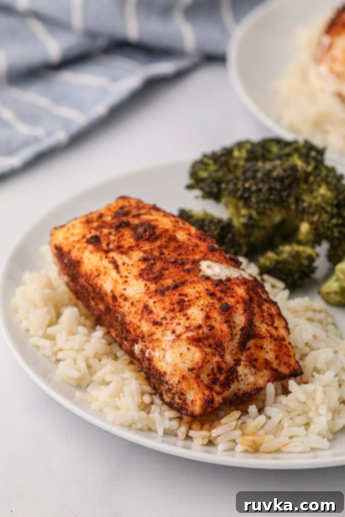 Perfect Air Fryer Halibut 2 Juicy seasoned halibut fillet on a white plate served with rice and broccoli, ready to eat
