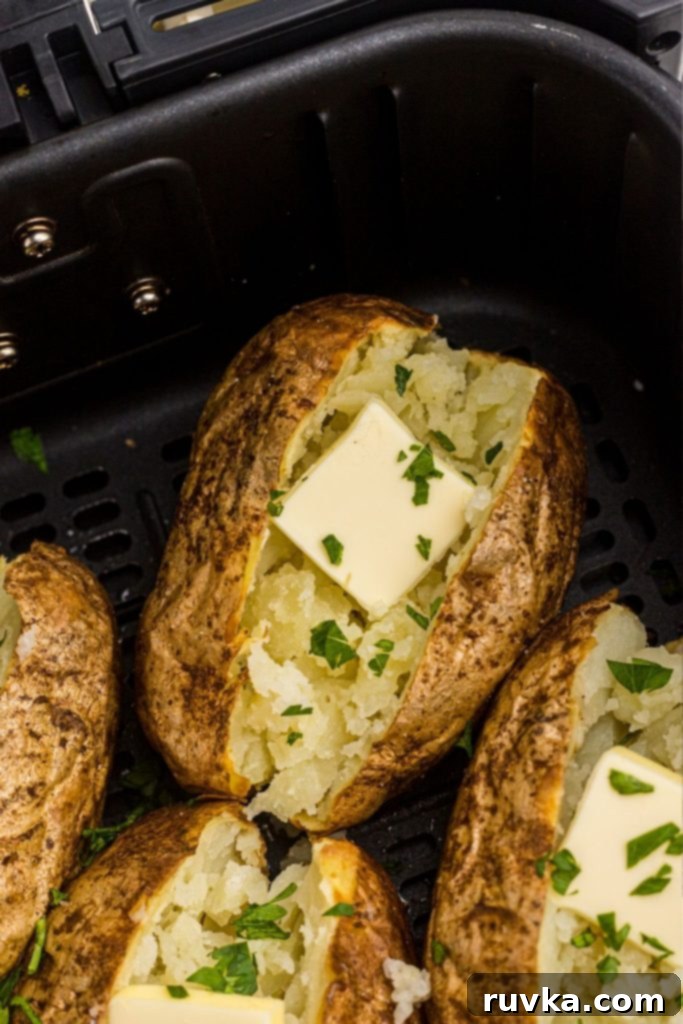 The Ultimate Air Fryer Baked Potato 2 Crispy baked potato in the air fryer basket, topped with butter.