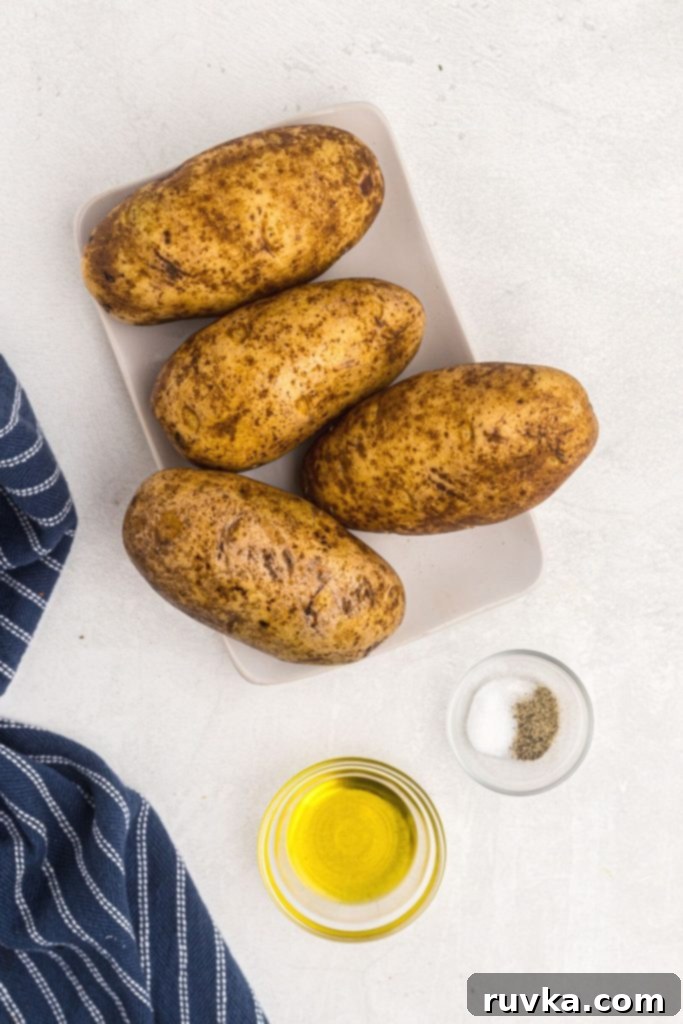 The Ultimate Air Fryer Baked Potato 3 Ingredients to make baked potatoes, olive oil, salt and pepper on a white marble table.