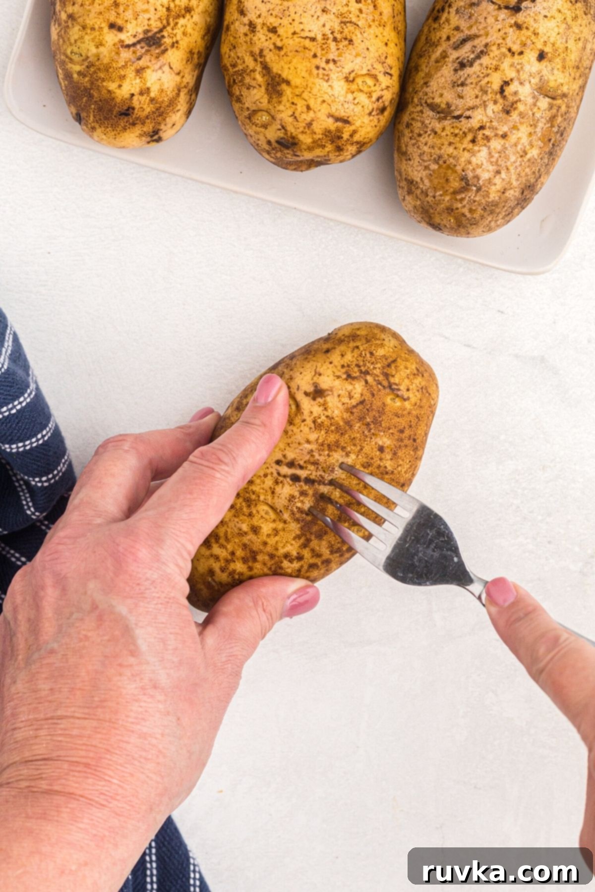 The Ultimate Air Fryer Baked Potato 4 Brown russet potatoes being pierced with a fork