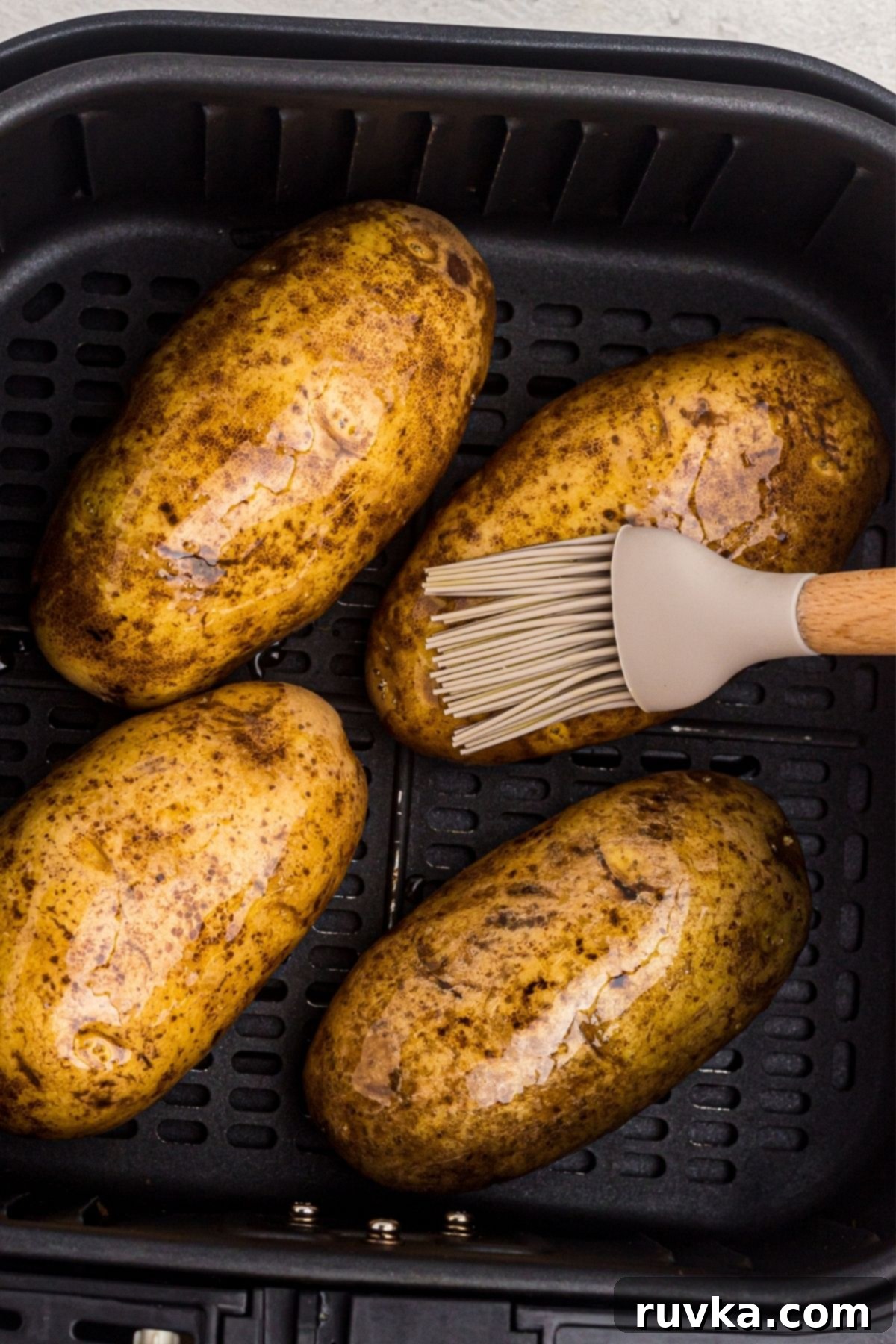 The Ultimate Air Fryer Baked Potato 5 Four potatoes in the air fryer basket being brushed with olive oil