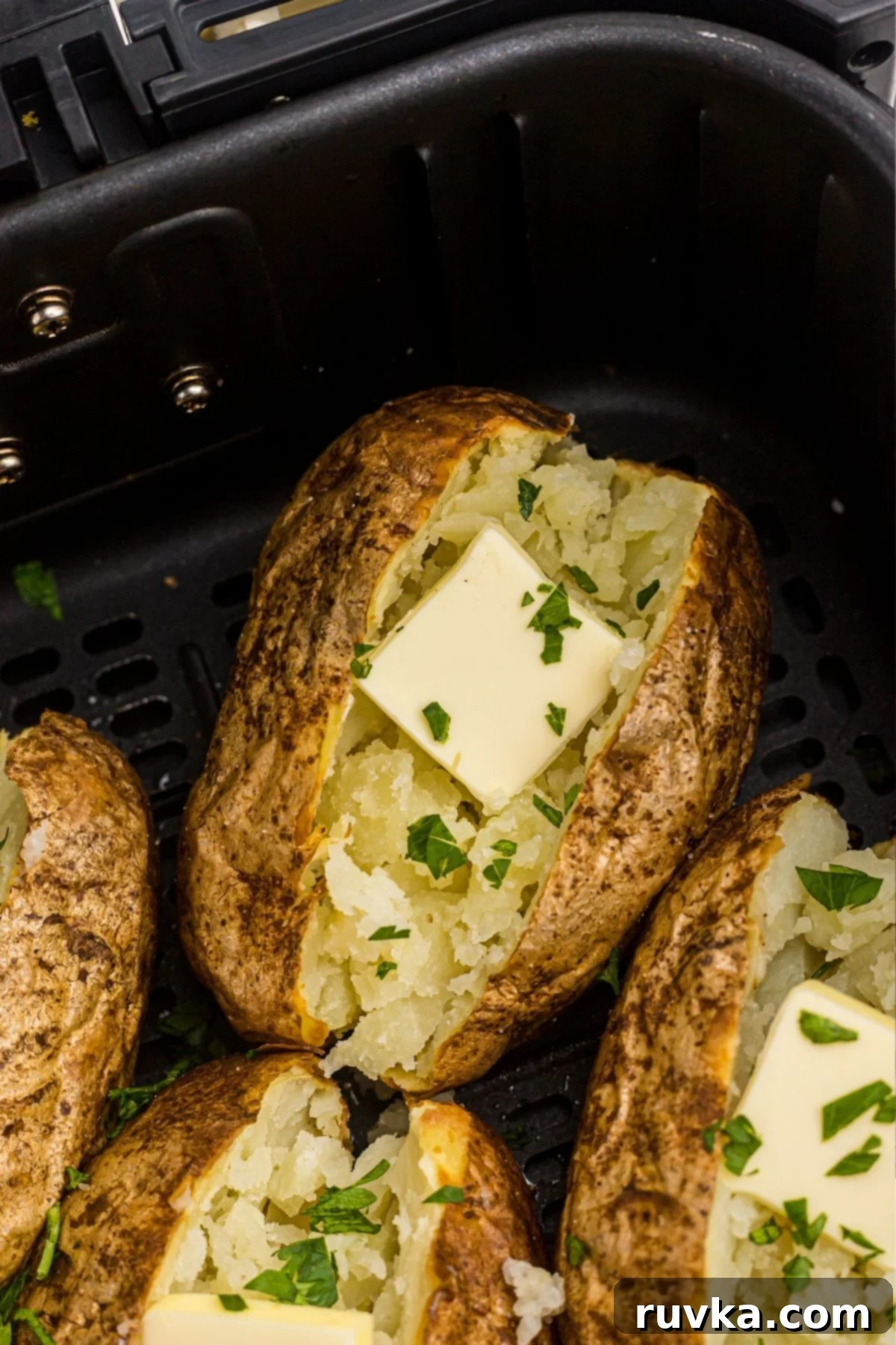 The Ultimate Air Fryer Baked Potato 7 Crispy baked potato in the air fryer basket, topped with butter.