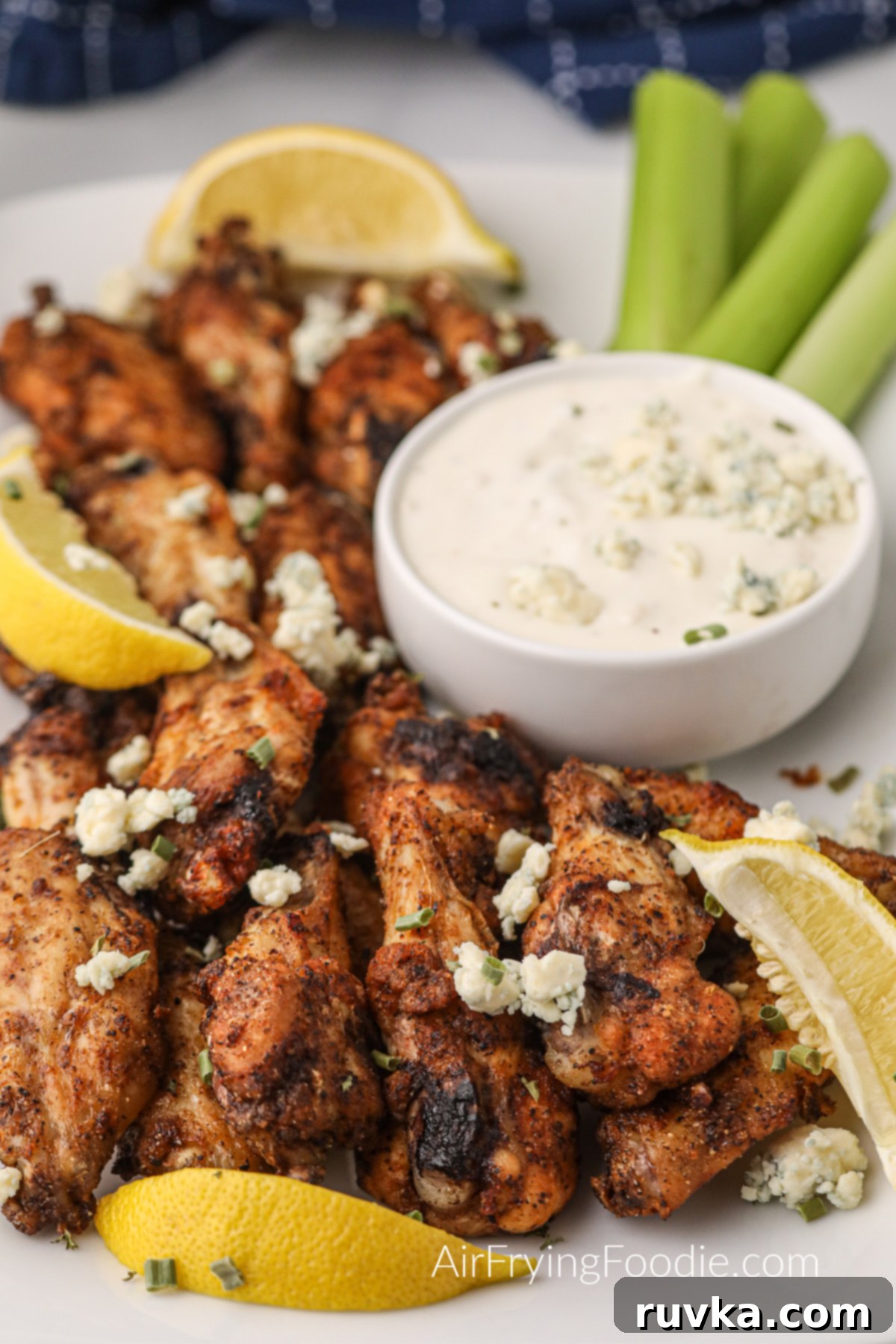 Zesty Air-Fried Lemon Pepper Wings 2 Crispy Air Fryer Lemon Pepper Wings on a white serving plate with fresh lemon wedges and blue cheese crumbles, ready to be enjoyed.