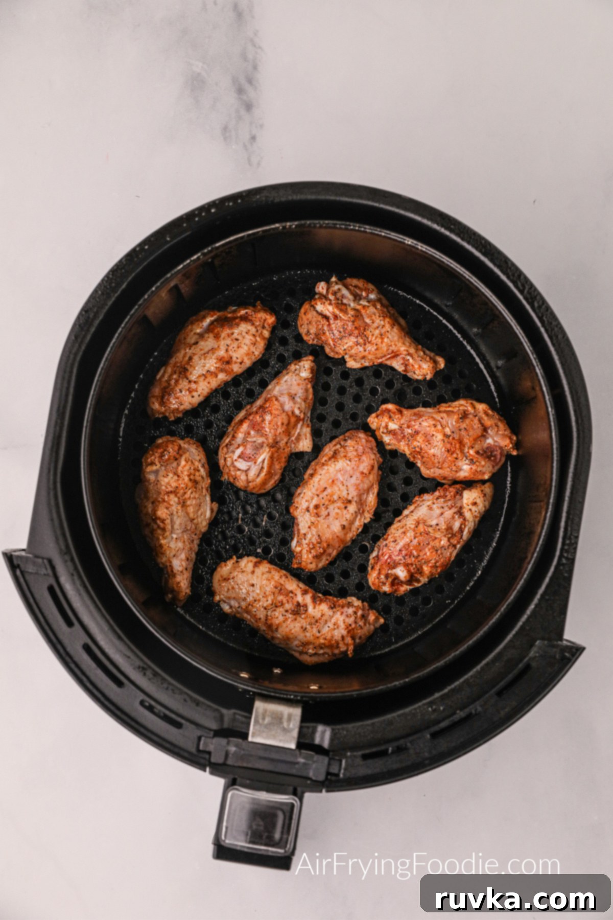 Zesty Air-Fried Lemon Pepper Wings 5 Perfectly seasoned chicken wings arranged in a single layer inside the basket of an air fryer, ready for cooking.