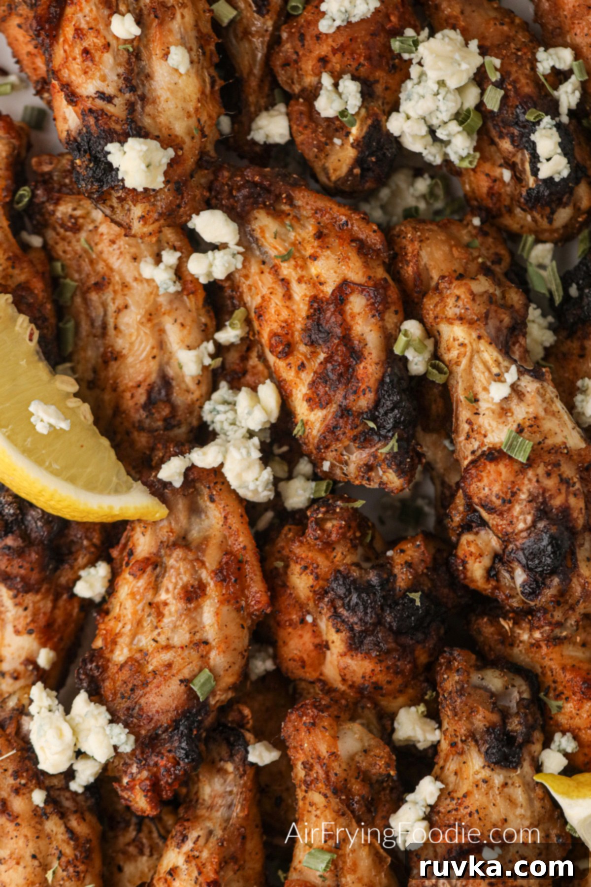 Zesty Air-Fried Lemon Pepper Wings 6 A mouth-watering closeup shot of golden-brown air fryer lemon pepper wings, garnished with fresh lemon wedges and blue cheese crumbles, showcasing their crispy texture.