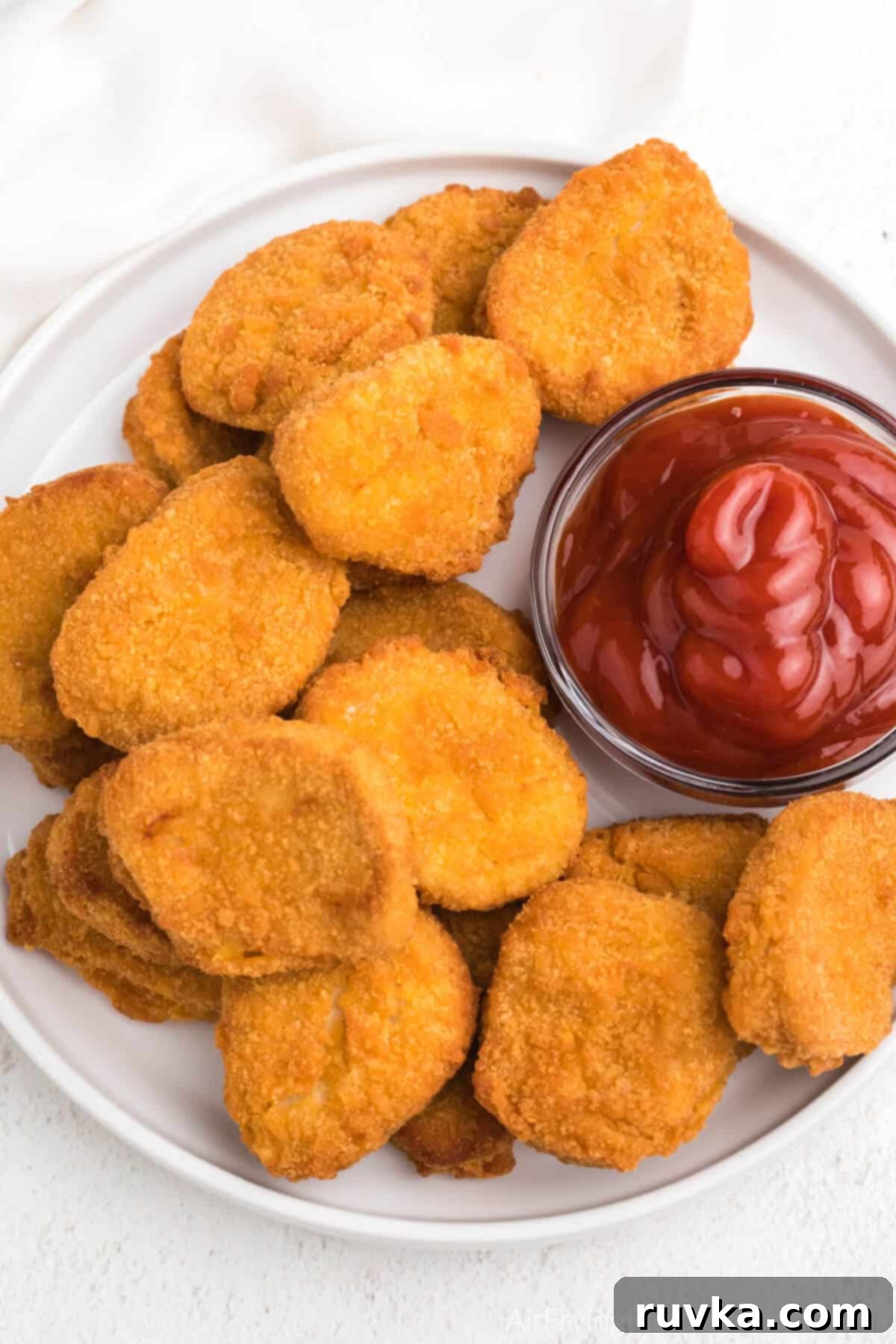 Golden Air Fryer Nugget Perfection 5 Perfectly cooked, golden-brown air fryer chicken nuggets served on a clean white plate with a side of bright red ketchup.