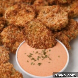 Crispy Air Fryer Fried Pickles 10 Air fried pickles being dipped into a creamy sauce, highlighting the crispy coating of the homemade fried pickles.