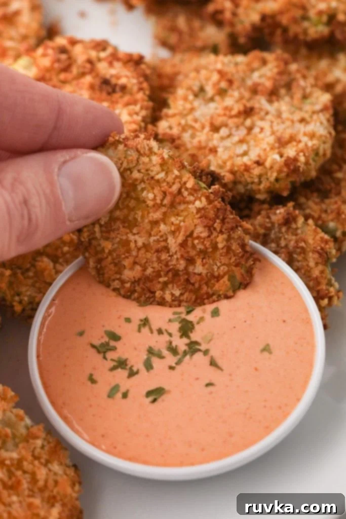 Crispy Air Fryer Fried Pickles 9 A perfectly battered and air-fried pickle chip being dipped into a creamy white sauce, showcasing its crispness.