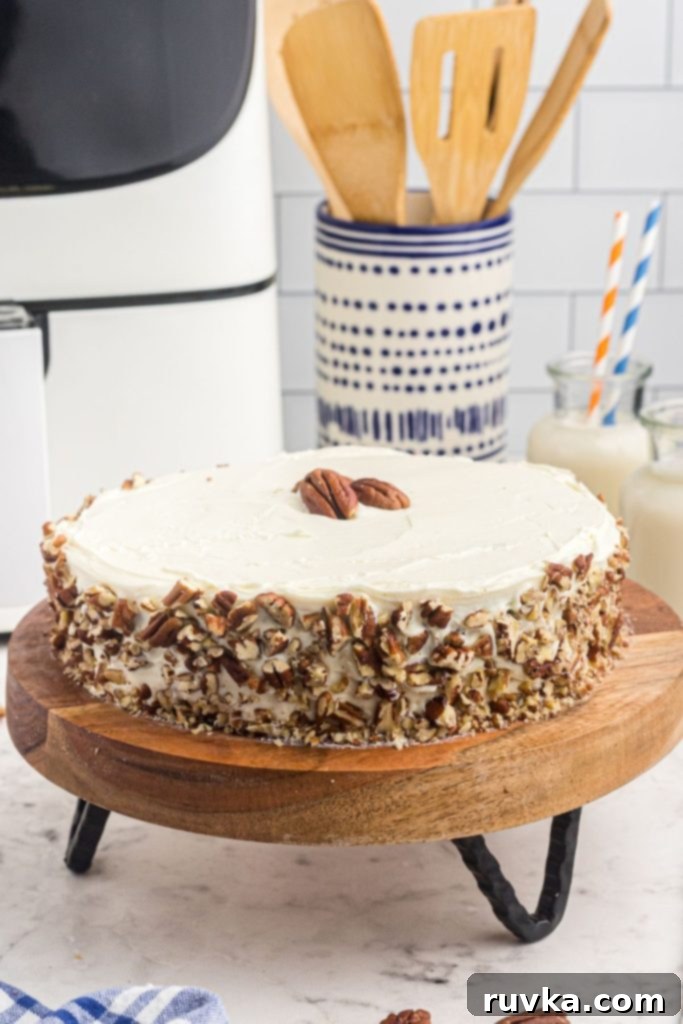 Air Fryer Carrot Cake Delight 4 Whole frosted cake on a cake stand in front of the air fryer