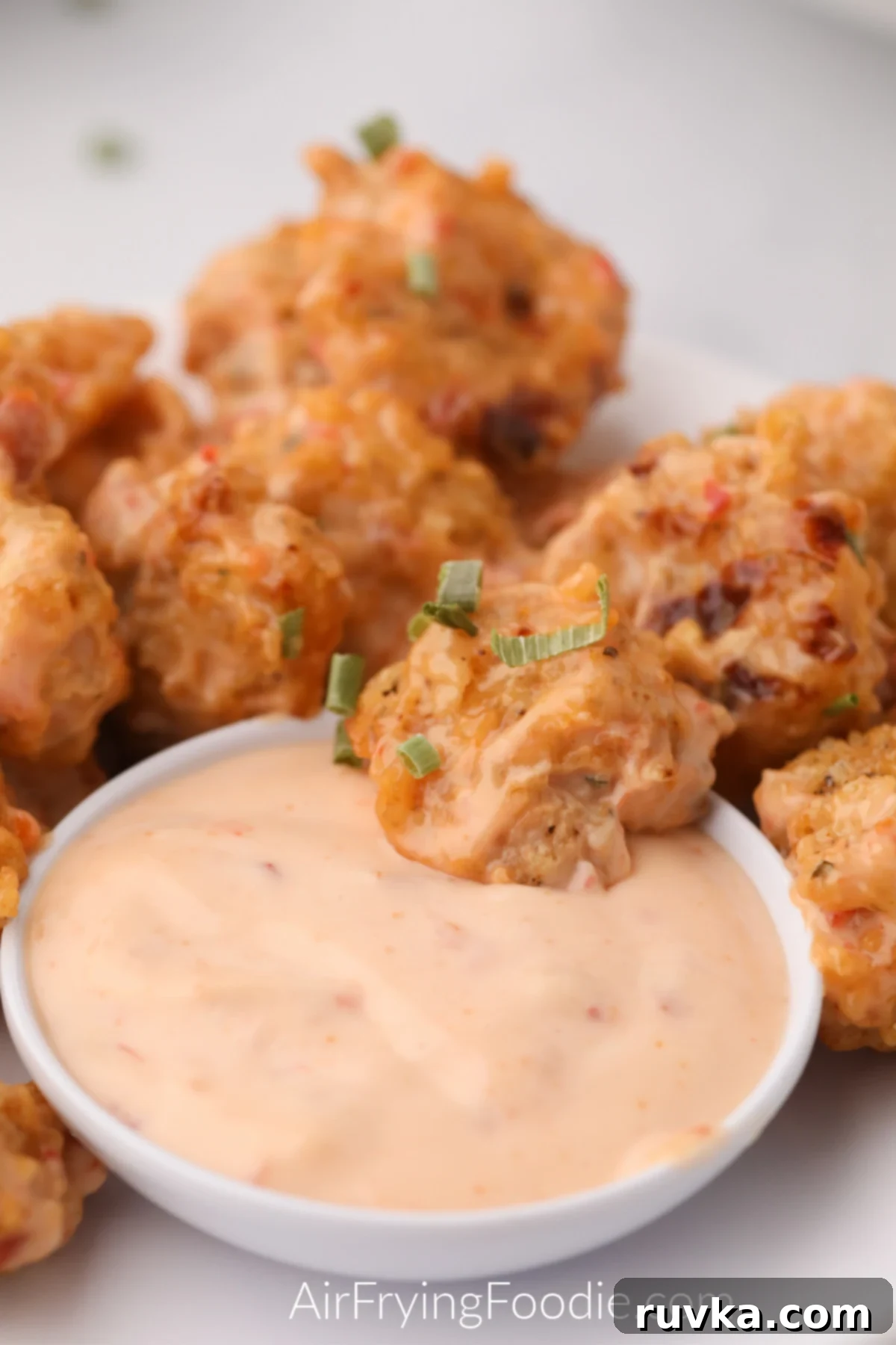 Crispy Air Fryer Bang Bang Shrimp 9 Close up shot of air fryer bang bang shrimp in dipping sauce, surrounded by a plate of air fryer bang bang shrimp.