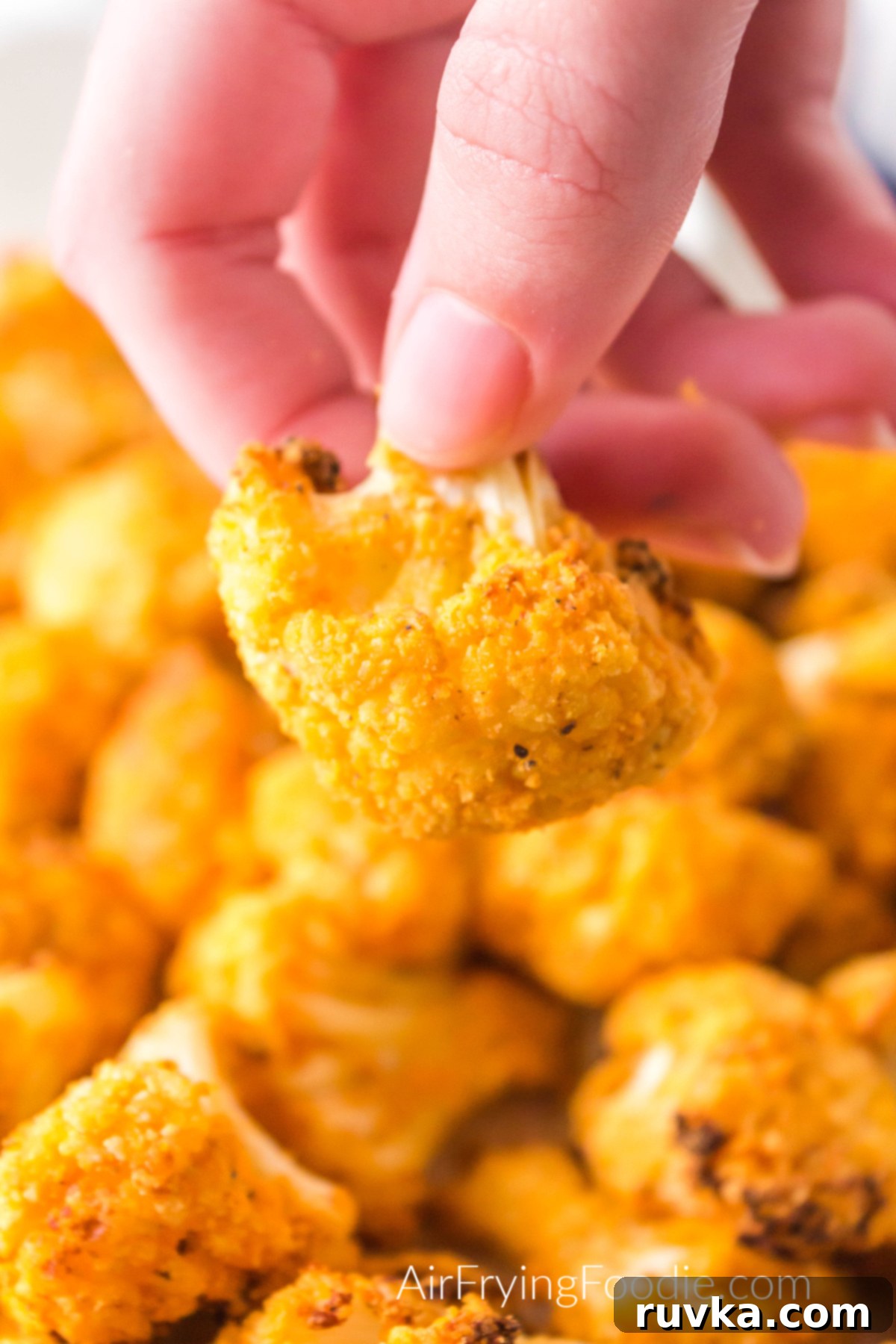 Spicy Air Fryer Cauliflower Wings 2 Air Fryer Buffalo Cauliflower on a white plate with a hand holding up a piece to eat.