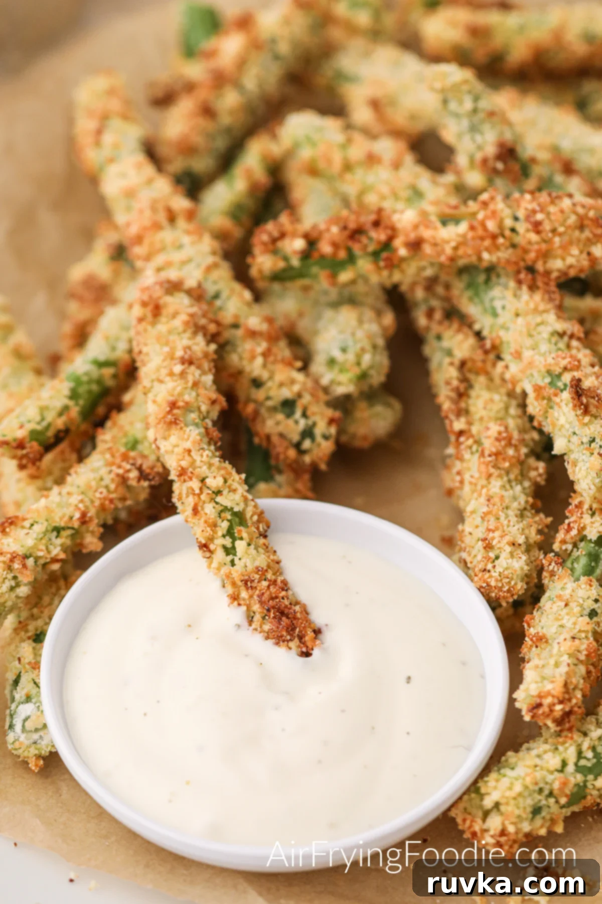 Air Fryer Crispy Green Bean Sticks 2 Crispy Air Fried Green Bean Fries arranged on a rustic wooden board with a small bowl of creamy dipping sauce.