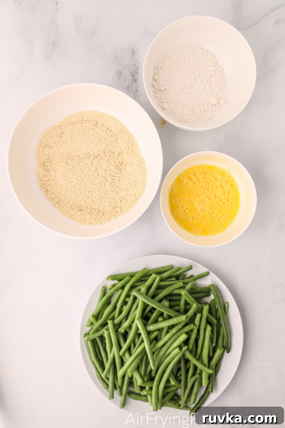 Air Fryer Crispy Green Bean Sticks 4 The initial setup for breading green beans, with separate bowls for flour, whisked eggs, and the seasoned breadcrumb mixture.