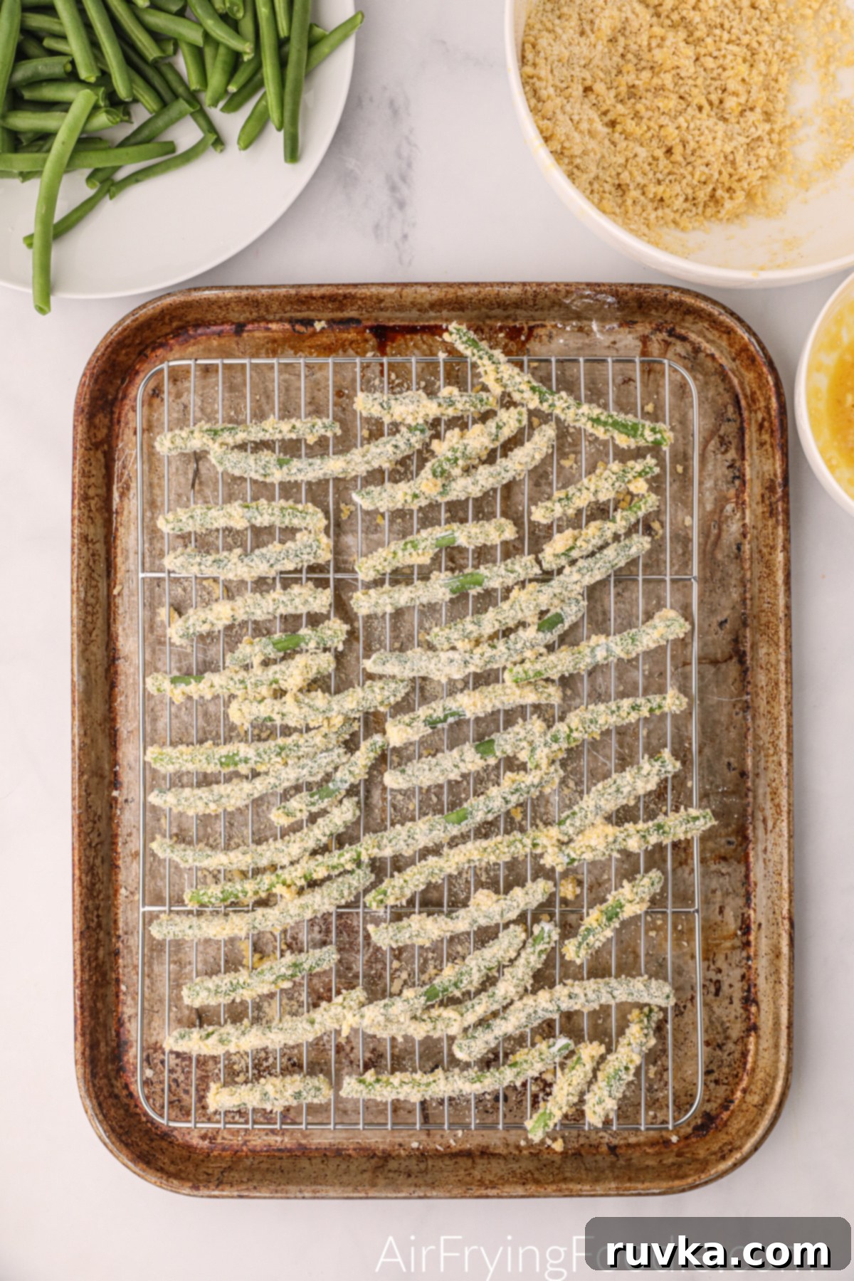 Air Fryer Crispy Green Bean Sticks 5 Flour, egg, and panko-coated green beans meticulously arranged on a cooling rack, lightly sprayed with olive oil, ready for the air fryer.