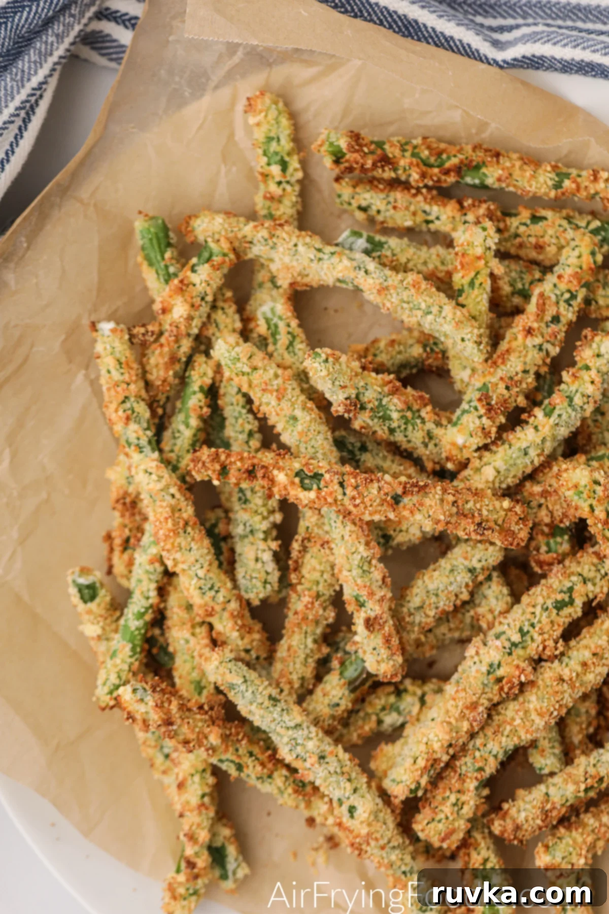 Air Fryer Crispy Green Bean Sticks 7 Freshly air fried green bean fries piled on a plate, garnished with fresh parsley and ready to be enjoyed with dipping sauce.