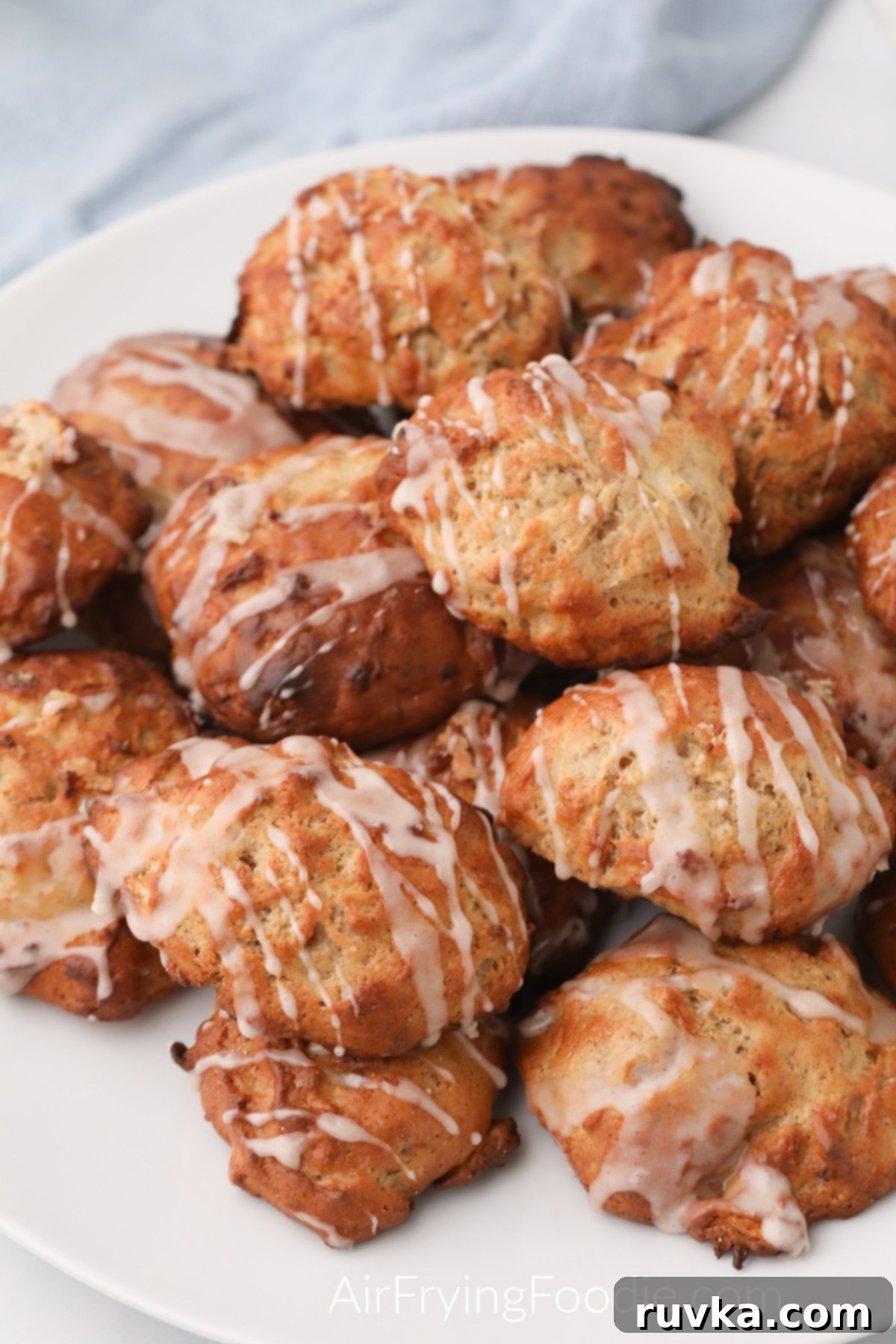 Easy Air Fryer Apple Fritters 2 Glazed air fryer apple fritters stacked high on a white plate, ready to be served and enjoyed as a delicious dessert.
