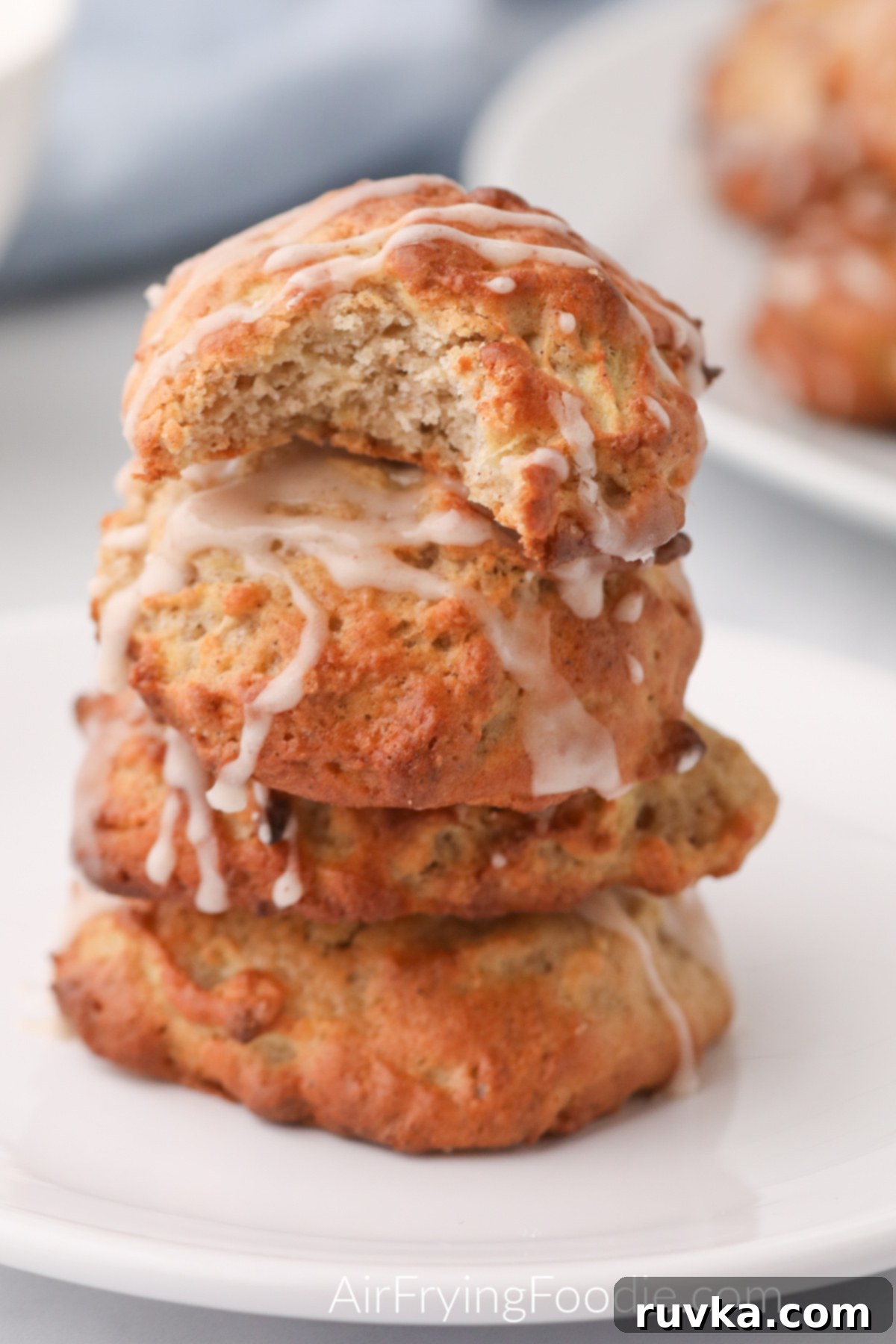 Easy Air Fryer Apple Fritters 11 A close-up of air fryer apple fritters stacked on a white plate, with a bite taken out of one to show the tender apple-filled interior, all covered in a sweet glaze.