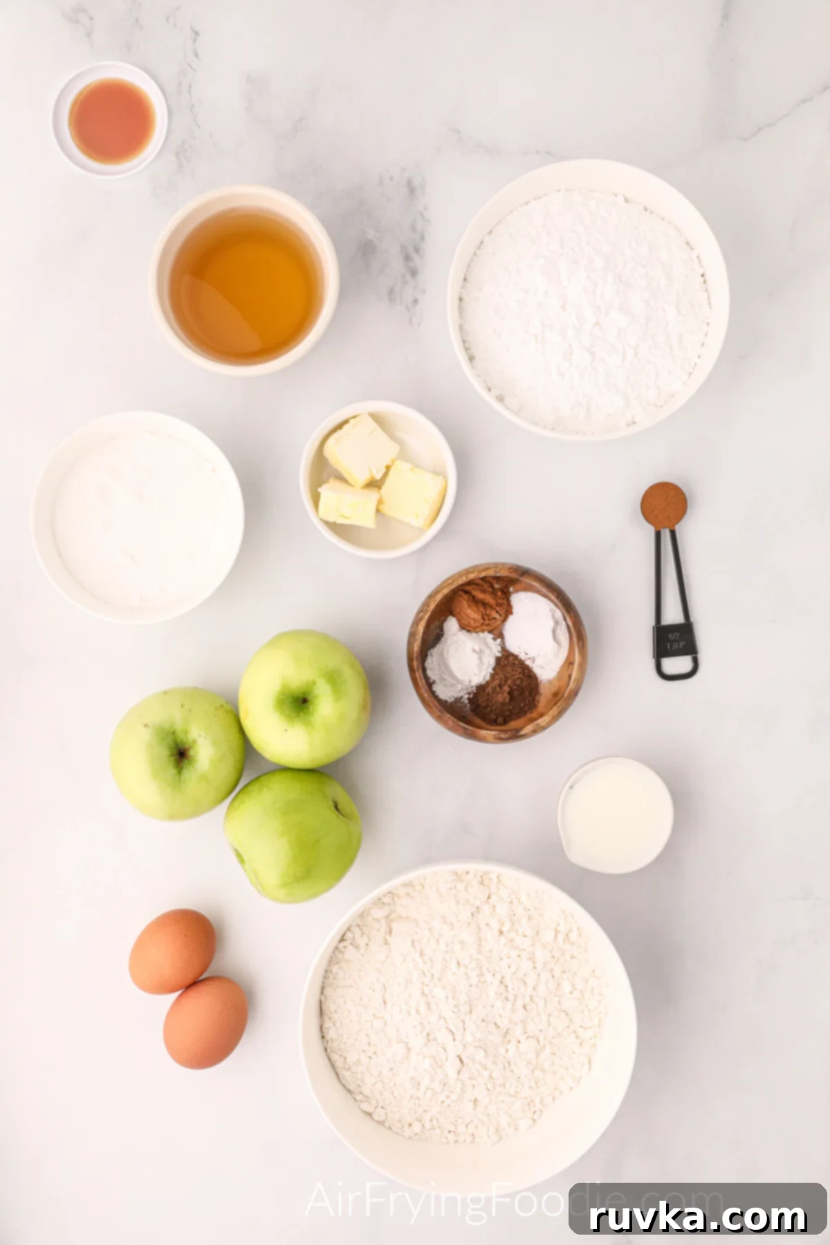 Easy Air Fryer Apple Fritters 3 All ingredients for homemade air fryer apple fritters, including apples, flour, sugar, spices, eggs, butter, and glaze ingredients, neatly arranged on a kitchen counter.