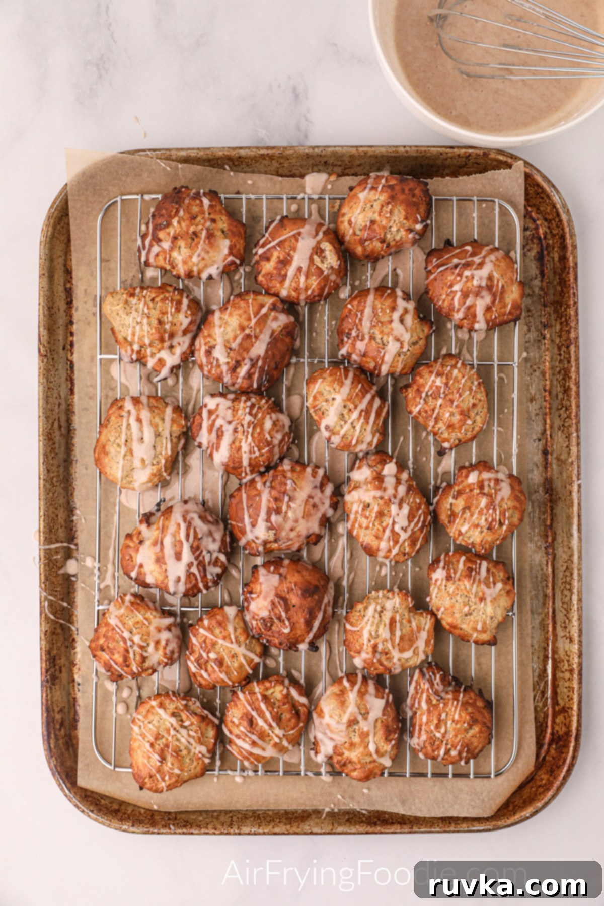 Easy Air Fryer Apple Fritters 8 Warm apple fritters cooling on a wire rack, drizzled with a sweet glaze, creating a beautiful and delicious topping.