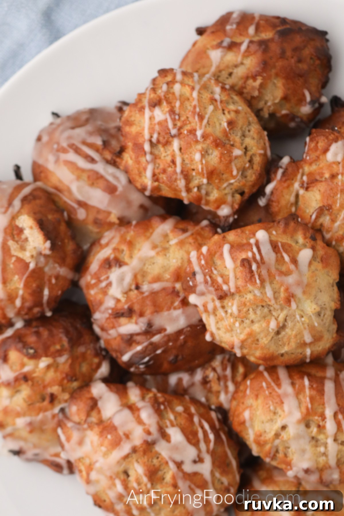 Easy Air Fryer Apple Fritters 10 An overhead view of air fryer apple fritters neatly arranged on a white plate, generously drizzled with sweet glaze and garnished with cinnamon.