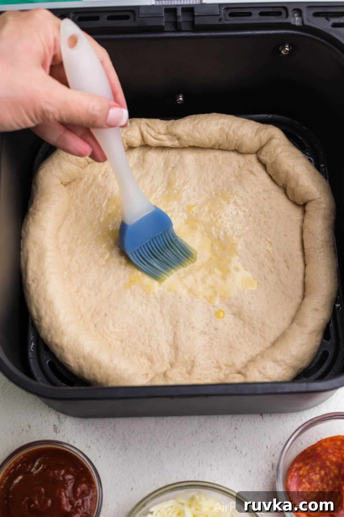 Crispy Air Fryer Pizza 5 Pizza dough being brushed with olive oil inside an air fryer basket, a crucial step for a crispy crust.