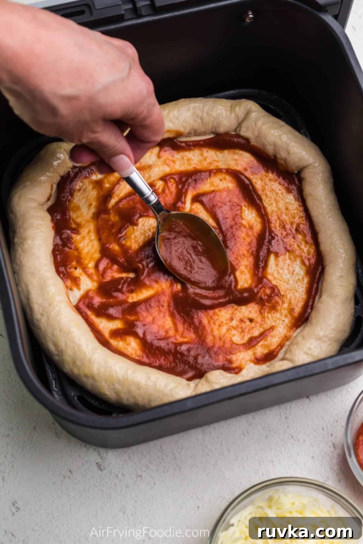 Crispy Air Fryer Pizza 6 Pizza sauce being spooned and carefully spread onto the air fryer pizza crust, ensuring an even layer.