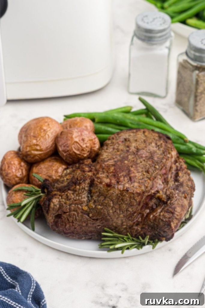 Perfect Air Fryer Beef Tenderloin 3 Juicy brown beef tenderloin on a white plate with potatoes and green beans in front of the air fryer.