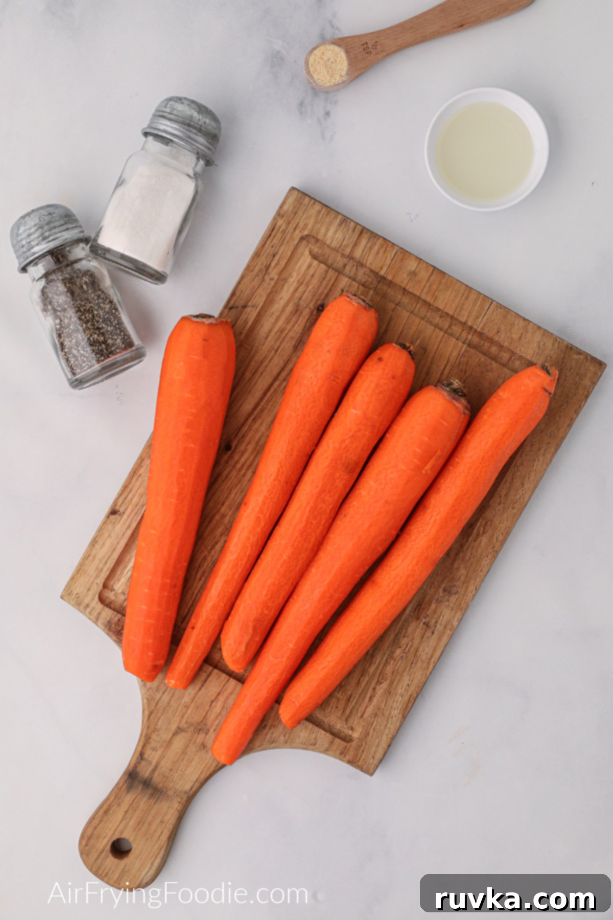 Crispy Air Fryer Carrot Fries 3 Ingredients on a white table and carrots on a cutting board.