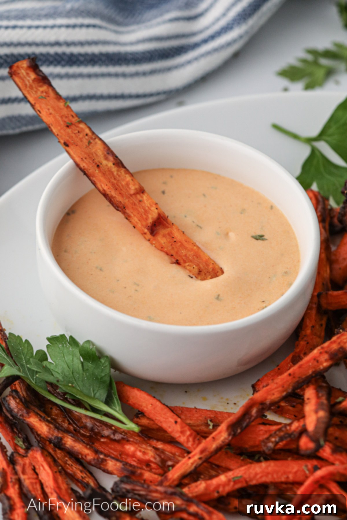 Crispy Air Fryer Carrot Fries 8 Carrot fry being dipped in a sauce, with other carrot fries on a plate.