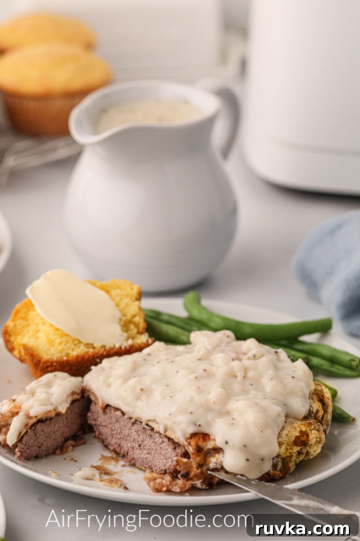 Crispy Air Fryer Chicken Fried Steak 2 Chicken fried steak made in the air fryer and served on a plate with green beans and cornbread.