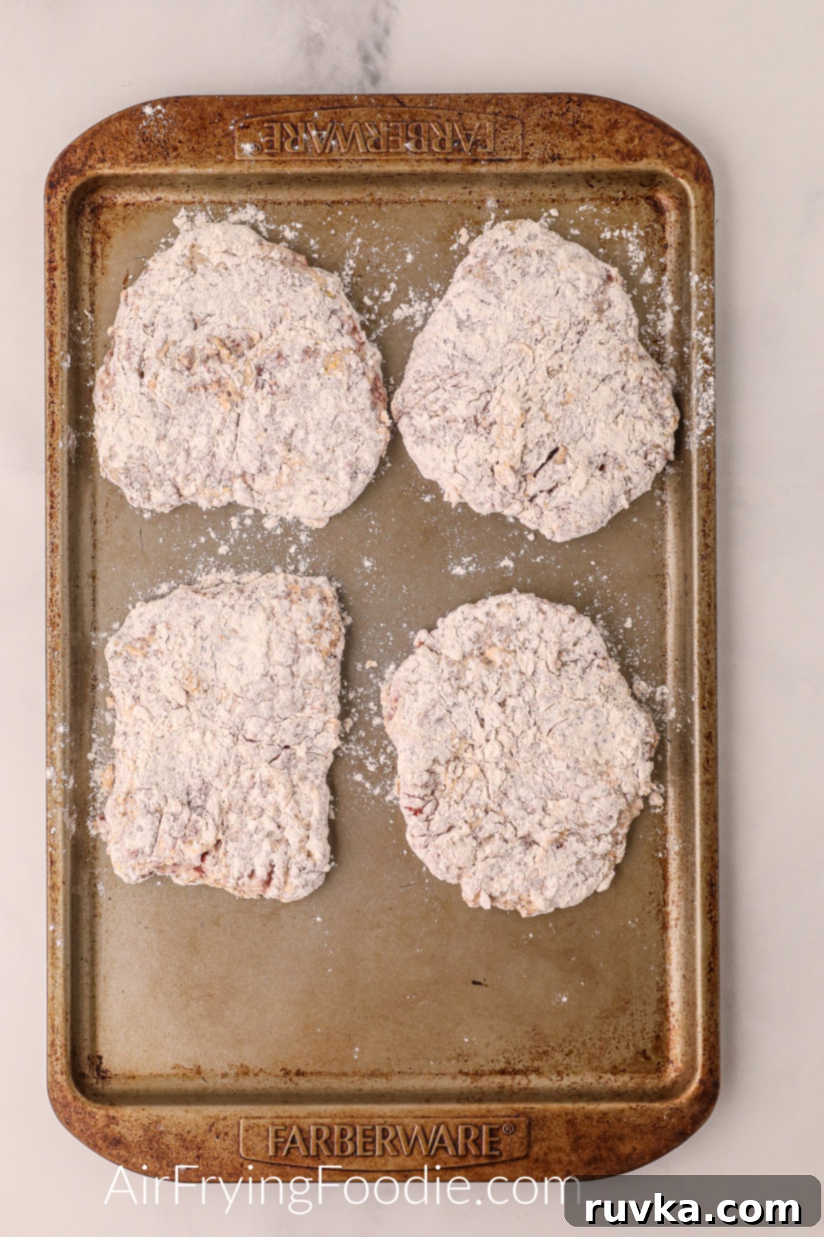 Crispy Air Fryer Chicken Fried Steak 5 Chicken fried steaks on a baking sheet, breaded and ready to be placed into the air fryer.