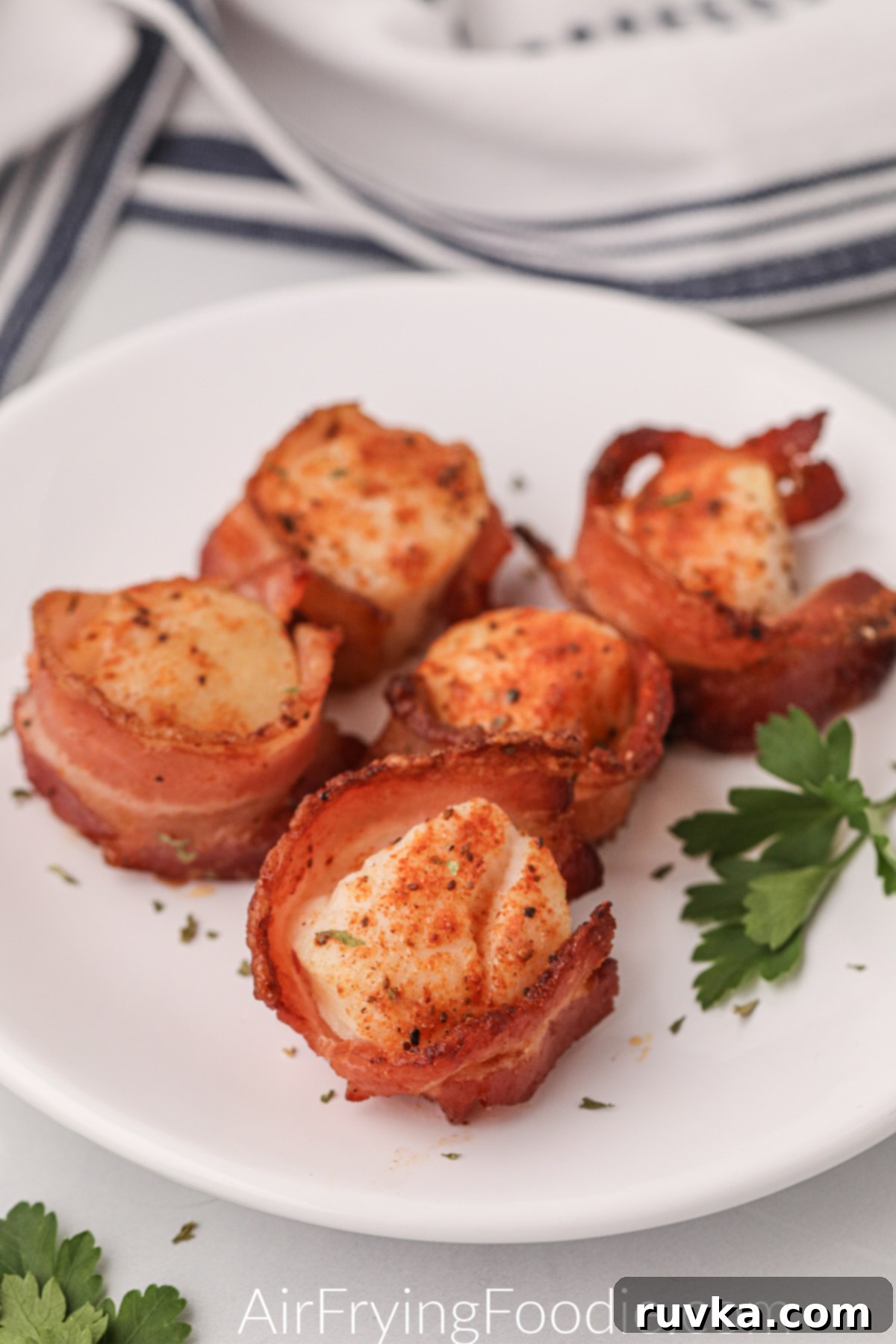 Crispy Air Fryer Bacon Wrapped Scallops 2 Air fryer bacon wrapped scallops fully cooked and on a white plate, ready to serve.