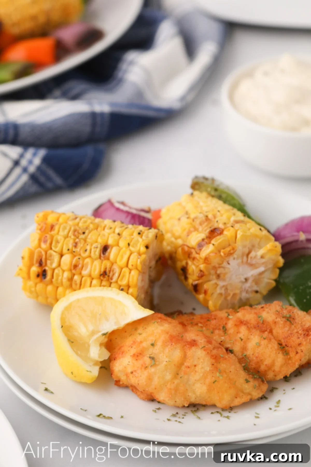Perfectly Crispy Air Fryer Catfish 2 Air Fried Catfish on a plate with corn and vegetables and a lemon wedge.