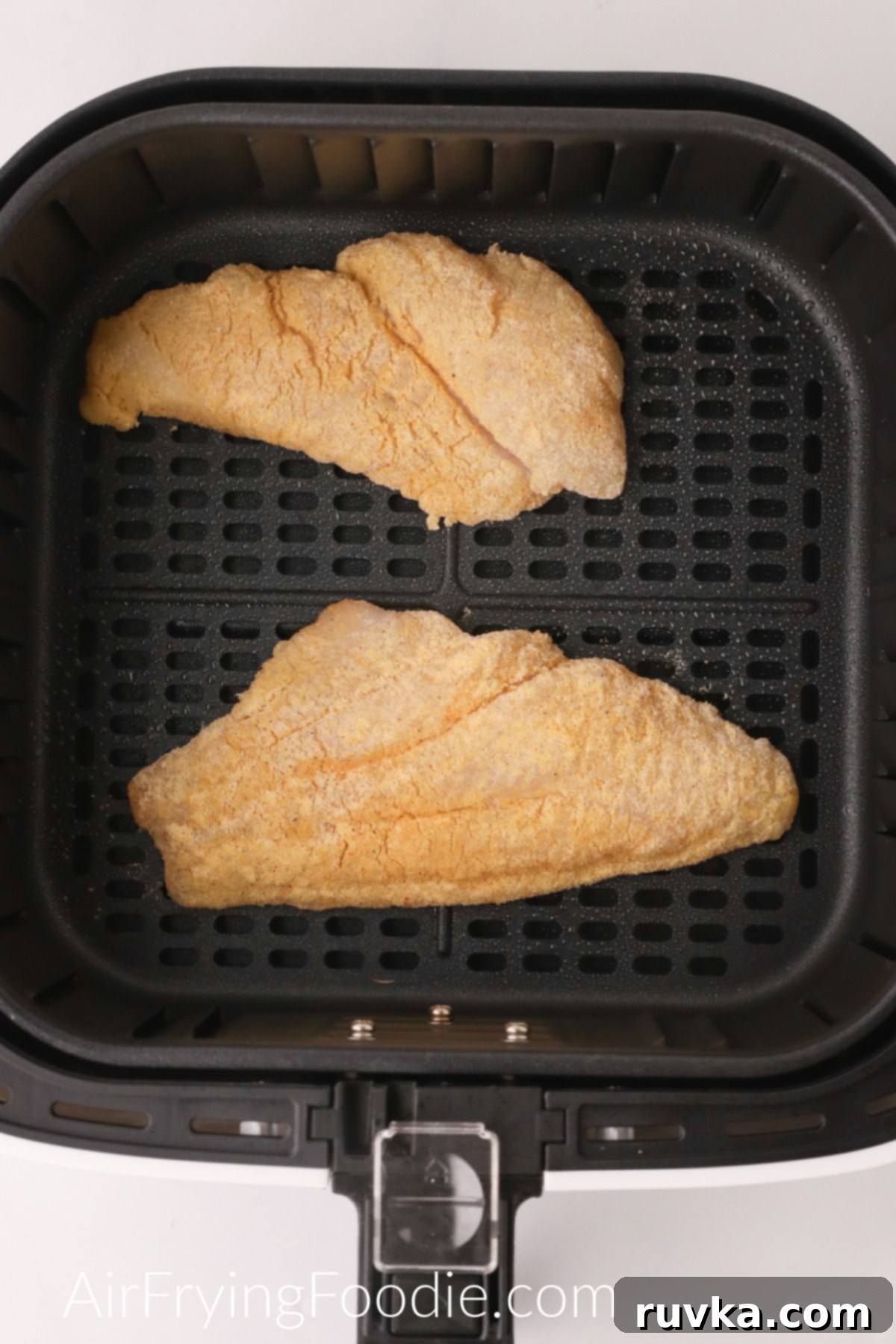 Perfectly Crispy Air Fryer Catfish 5 Breaded catfish fillets in the basket of the air fryer, ready to cook.