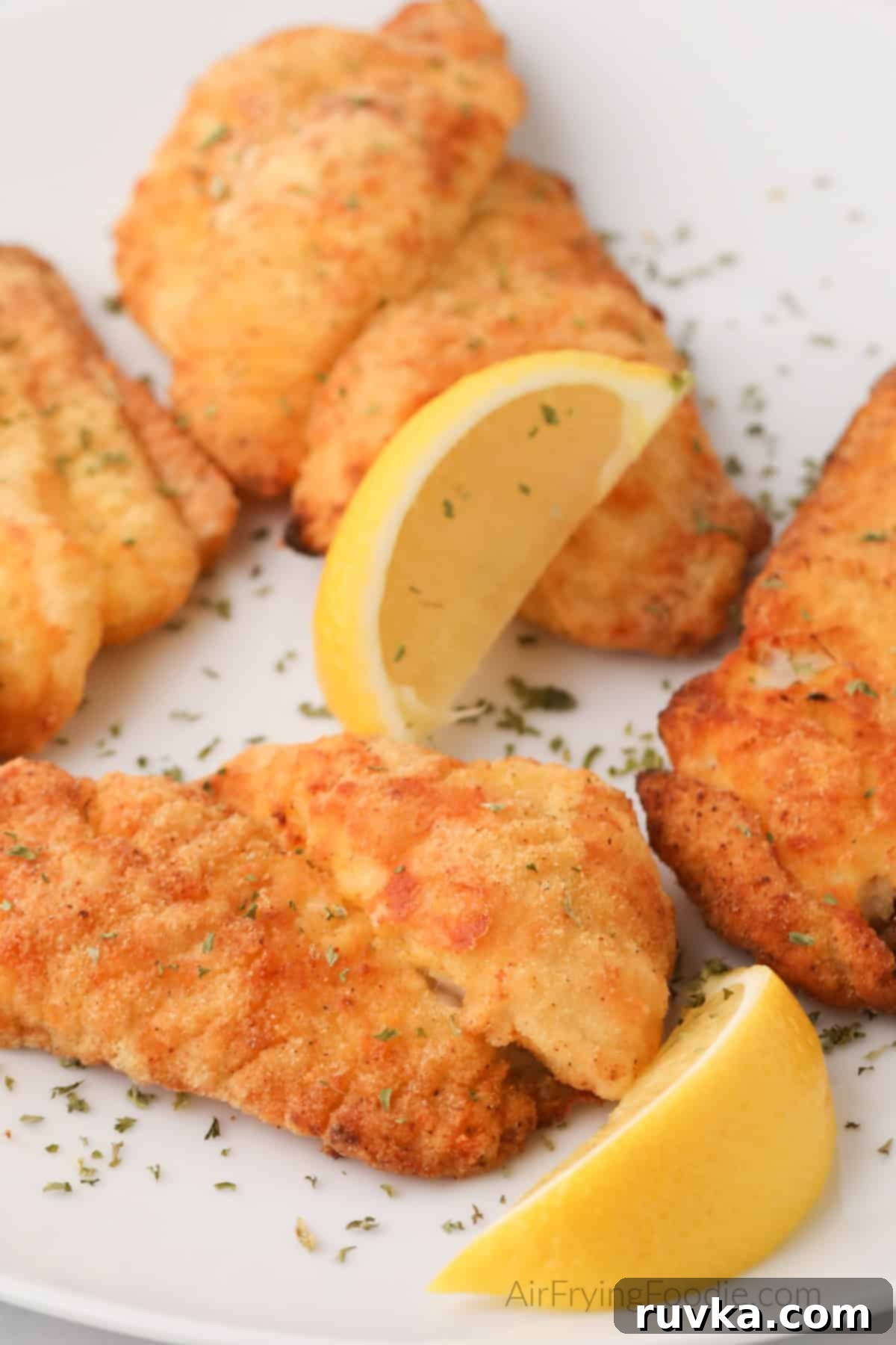 Perfectly Crispy Air Fryer Catfish 7 Air fried catfish filets on a white plate with lemon slices, ready to serve.