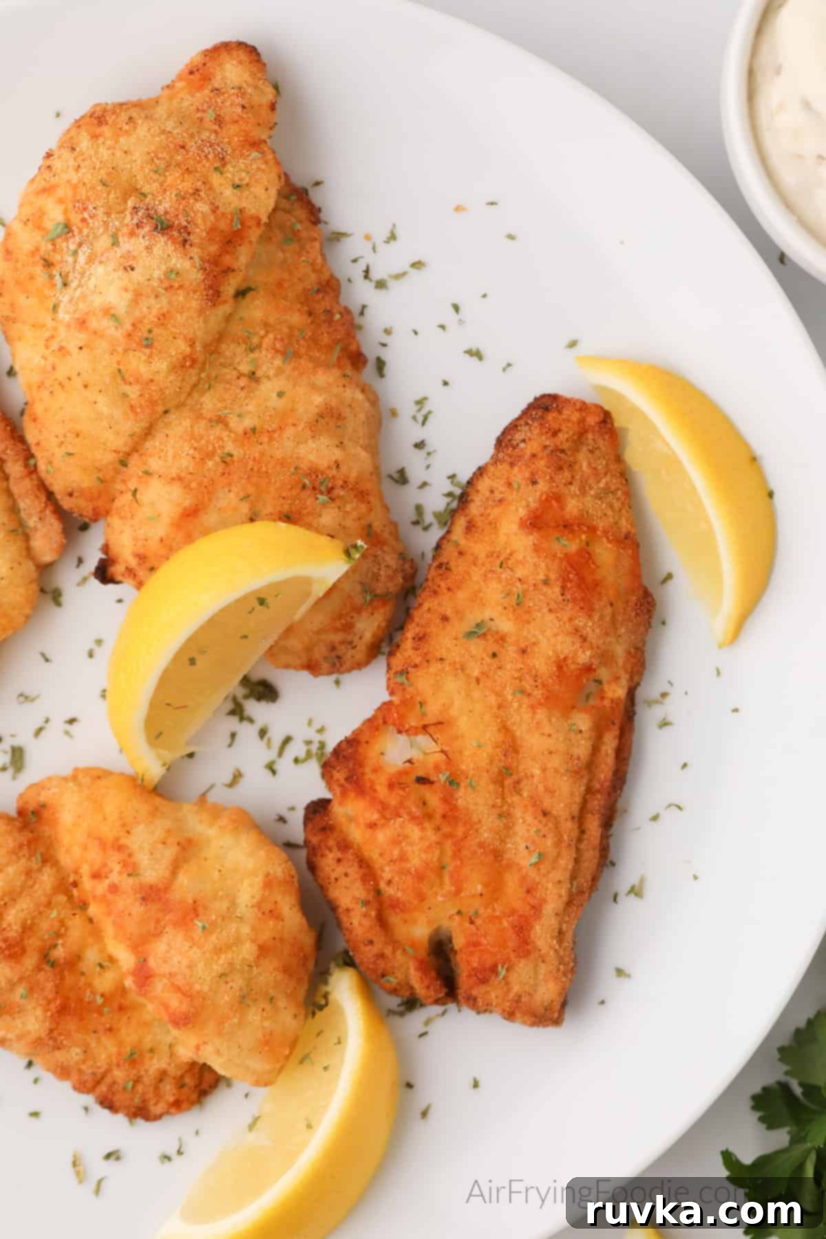 Perfectly Crispy Air Fryer Catfish 9 Air fried Catfish filets on a white plate with lemon wedges, ready to serve.