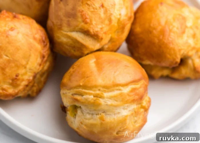 Air Fryer Biscuit Surprises 3 Close up of a batch of biscuit bombs on a white plate that are made with biscuit, egg, cheese, and bacon, and cooked in an Air Fryer. The inside is visible, showing the delicious filling.